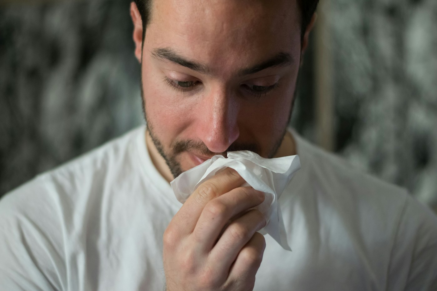A man in a white shirt holding a tissue to his nose