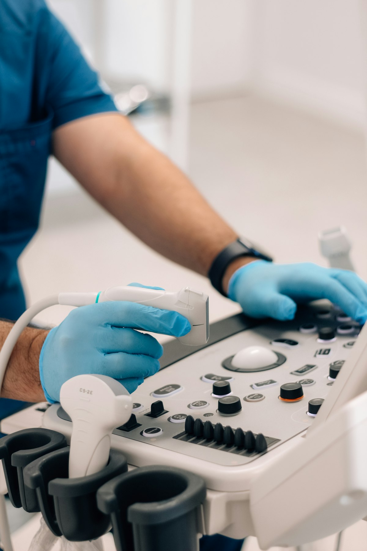 Gloved hands holding an ultrasound probe beside the scanner controls